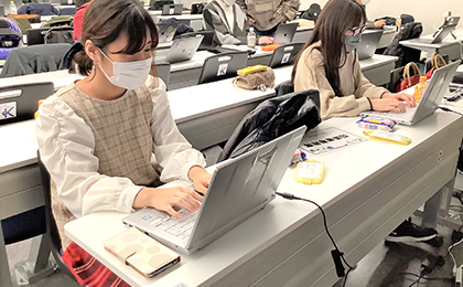 パソコンテイクの写真が表示されています。 授業中、学生サポーターの2人が横並びに座り、パソコンテイクをしている様子。