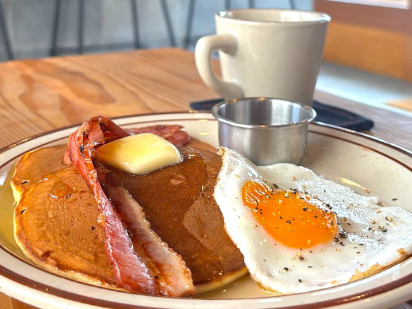 朝限定、ベーコンが乗ったパンケーキ「アメリカンブレックファスト」。横には目玉焼きとメープルシロップが添えられています。